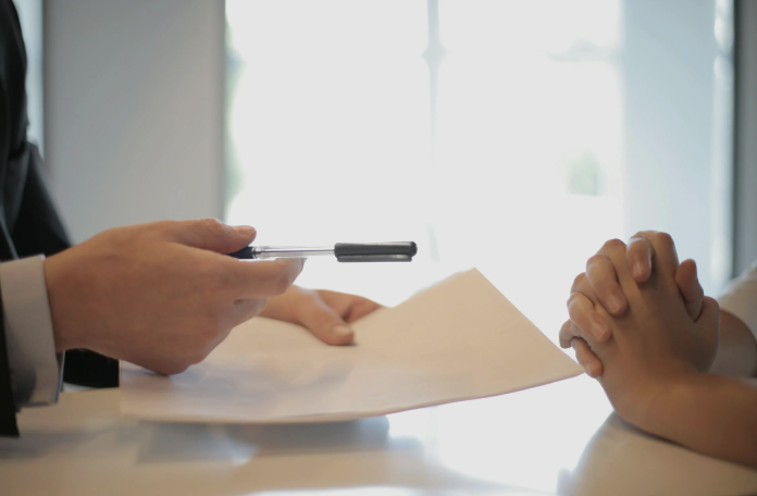 A man and woman sit at a table, engaged in writing with a pen and paper, focused on their task.