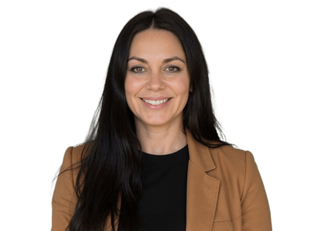 A woman with long black hair wearing a brown jacket stands confidently, showcasing her style and poise.