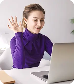 A woman sits at a desk, focused on her laptop, with a notepad and pen beside her.