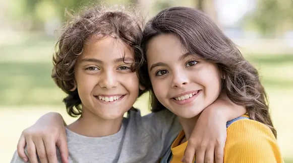 Two young children smile and embrace each other, radiating joy and affection in a warm, playful moment.