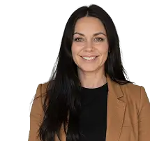 A woman with long black hair wearing a brown jacket stands confidently, showcasing her style and poise.