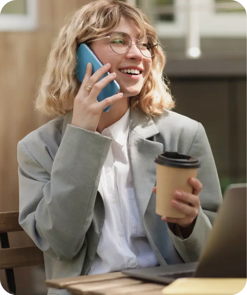 A professional woman in glasses and a suit, holding a coffee cup while engaged in a phone conversation.