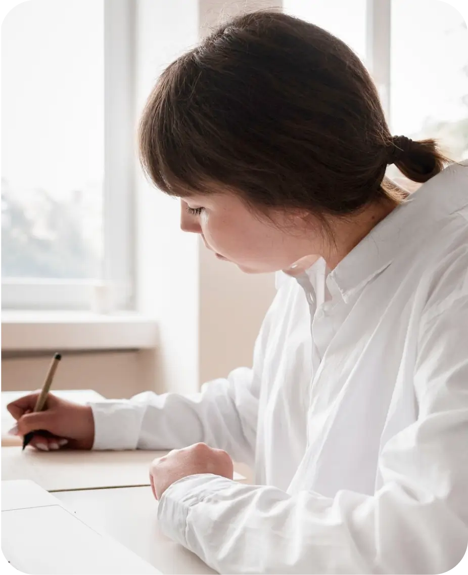 A woman dressed in a white shirt is engaged in writing on her laptop, illustrating a scene of concentration and creativity.