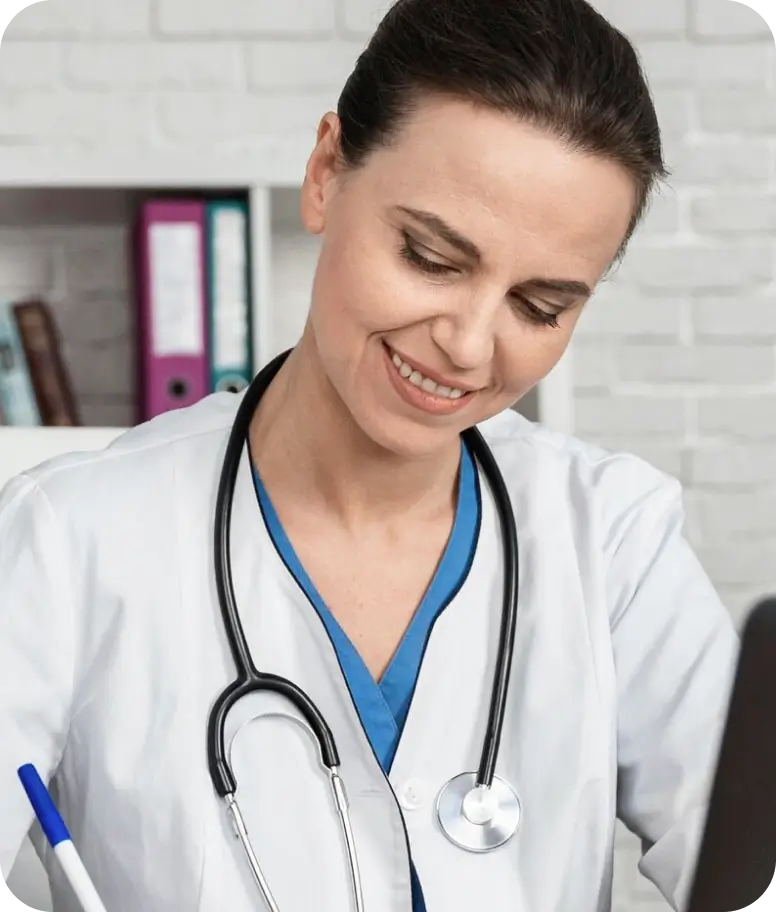 A woman in a white coat is focused on writing notes on a piece of paper at a desk.