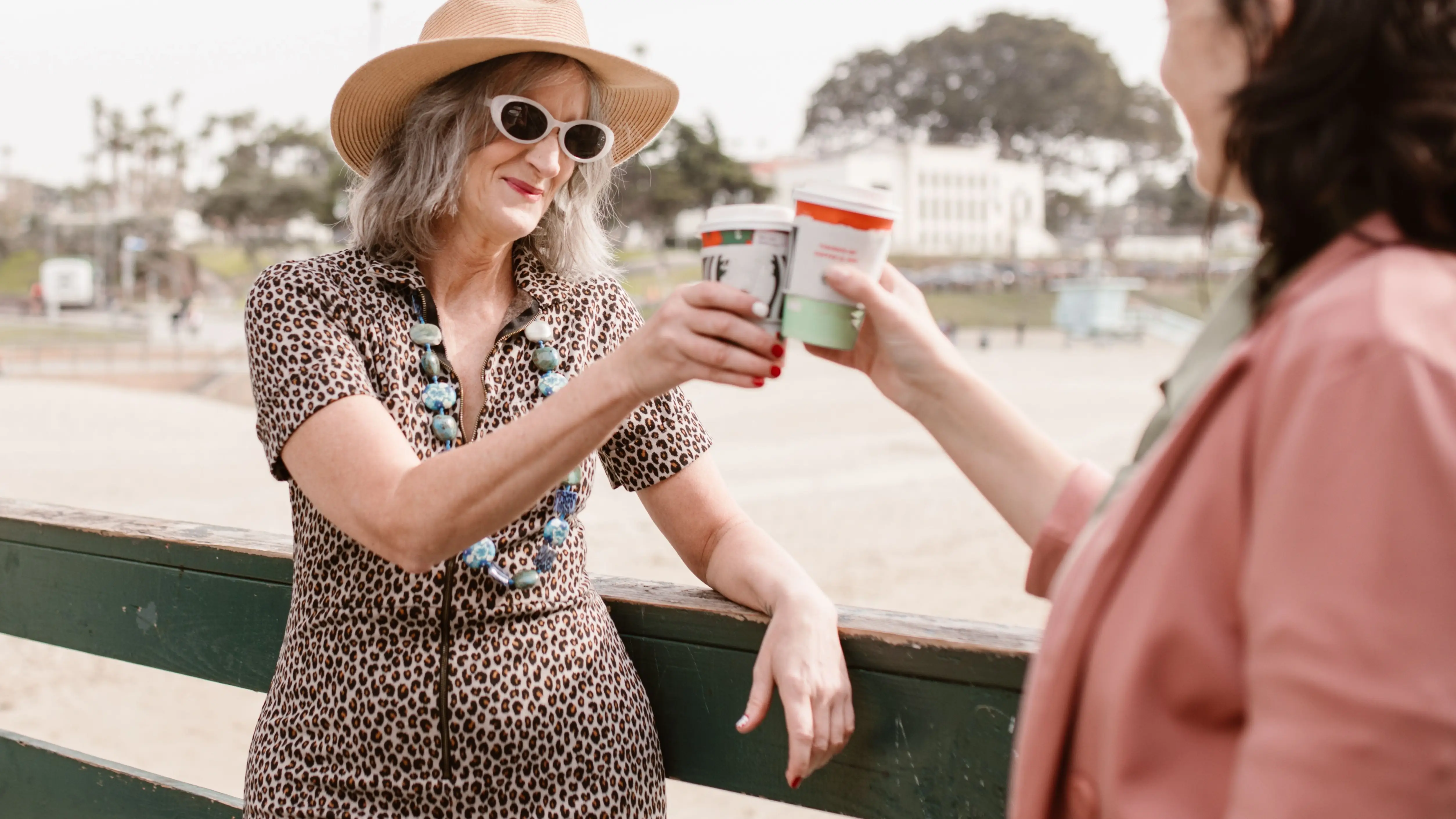 Two women enjoying coffee together outdoors on a sunny day, reflecting everyday wellbeing in midlife.