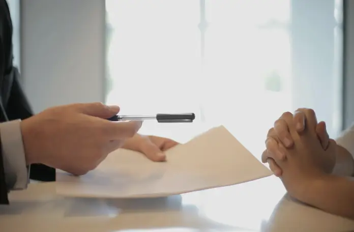 A man and woman sit at a table, engaged in writing with a pen and paper, focused on their task.