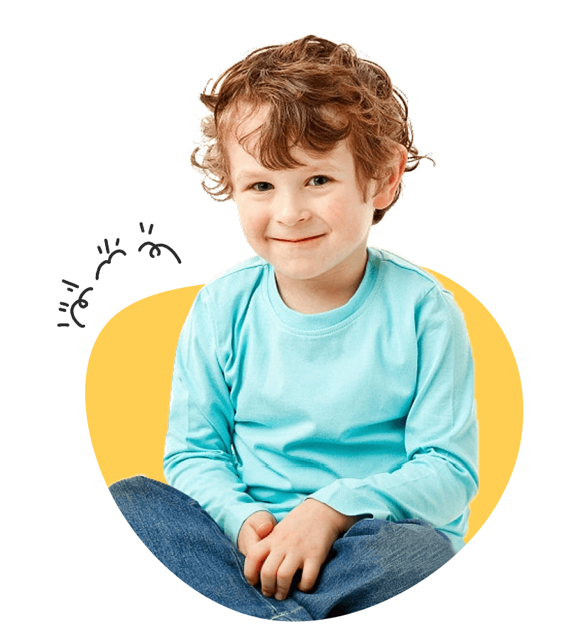 A young boy sits on the floor, hands in pockets, looking relaxed and contemplative.